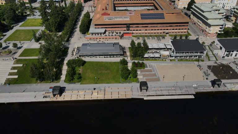 Flygbild över centrala Skellefteå med parkstråk, kajpromenad och Skellefteälven en sommardag