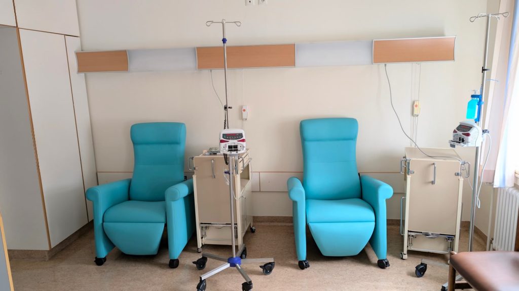 Ett tomt infusionsrum på ett sjukhus med två turkosa behandlingsstolar, droppställningar och infusionspumpar.